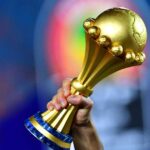 ** صورة لشعار كأس أمم أفريقيا، مع خلفية ملونة ورموز كرة القدم.