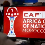 صورة للمباراة الافتتاحية بين منتخبي المغرب وجزر القمر، مع خلفية للملاعب والمشجعين.