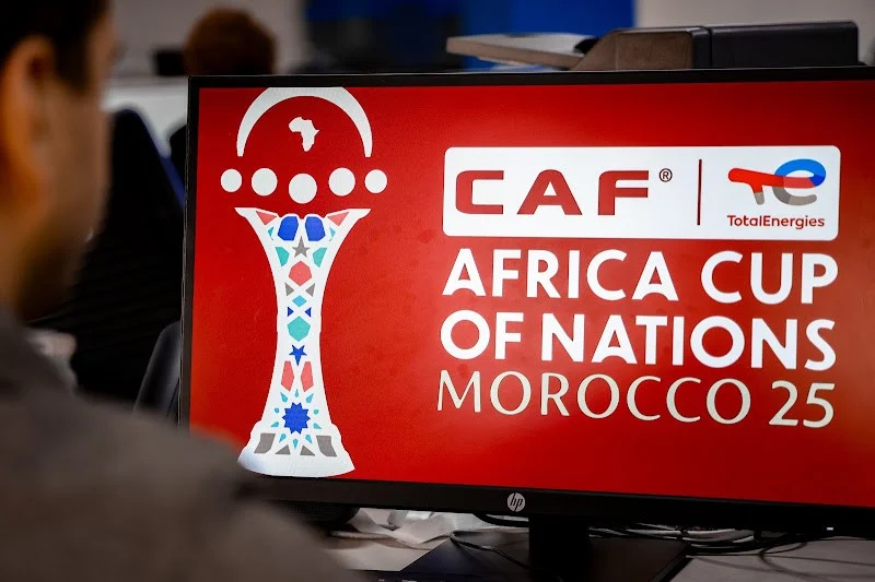 صورة للمباراة الافتتاحية بين منتخبي المغرب وجزر القمر، مع خلفية للملاعب والمشجعين.