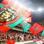 ** صورة للاعب كرة القدم يلعب مع رفاقه، مع خلفية ملونة وملونة بمعالم الرياضة الإفريقية.