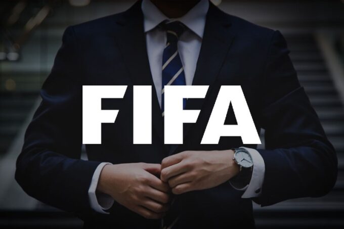 صورة للاعب كرة القدم يرتدي قميص نادي معين، مع وكلاء اللاعبين في الخلفية.