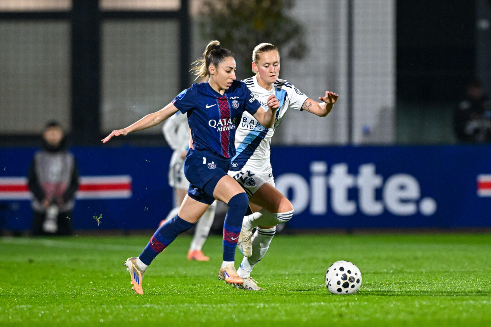 Les joueuses du Paris Saint-Germain et du Paris FC se disputent un ballon sur le terrain.