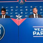 Le logo du Paris Saint-Germain avec Kylian Mbappé en arrière-plan.