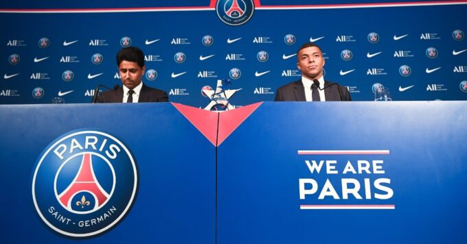 Le logo du Paris Saint-Germain avec Kylian Mbappé en arrière-plan.