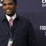 Samuel Eto'o, président de la Fecafoot, souriant devant le drapeau camerounais.