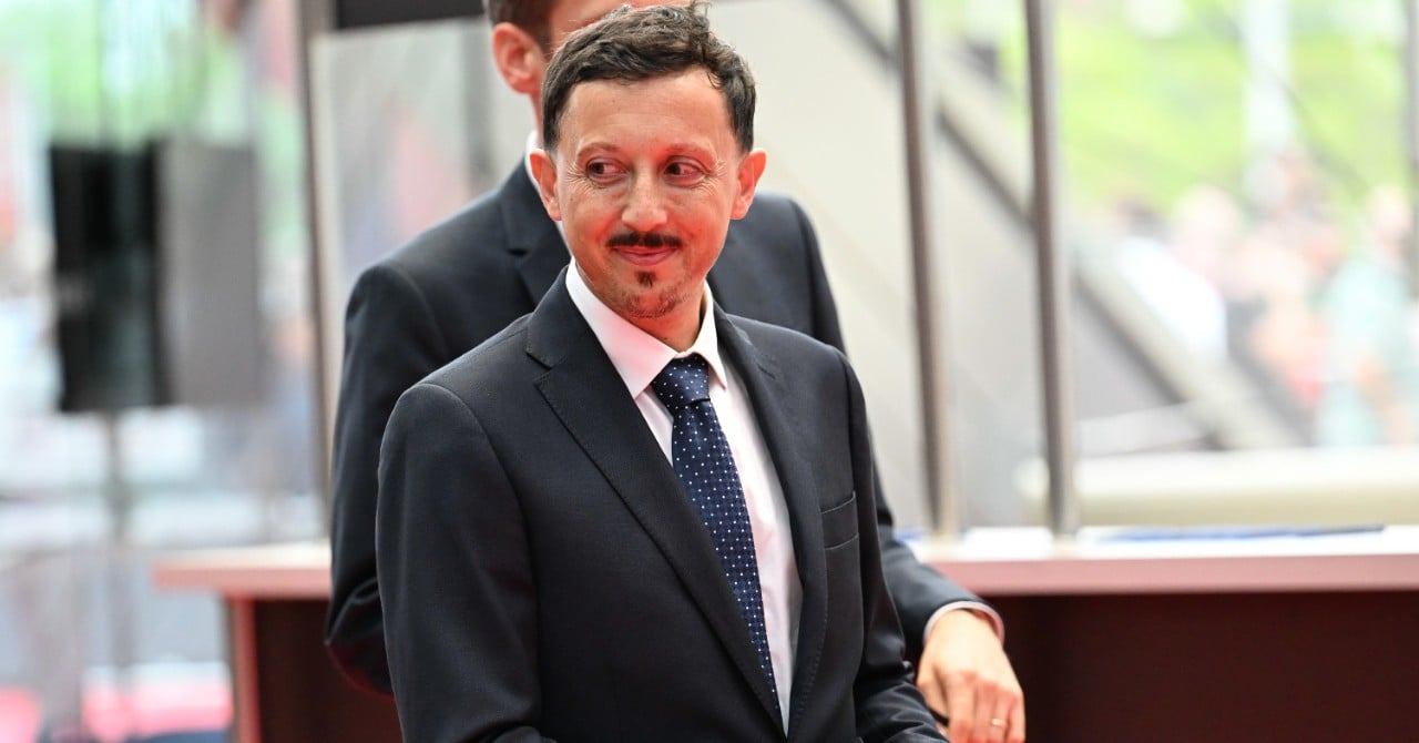 Joueur de football en action, avec des ballons et des supporters en arrière-plan.