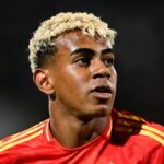 Spain's 2026 World Cup home kit with deep red body, navy sleeves, and yellow pinstripes.